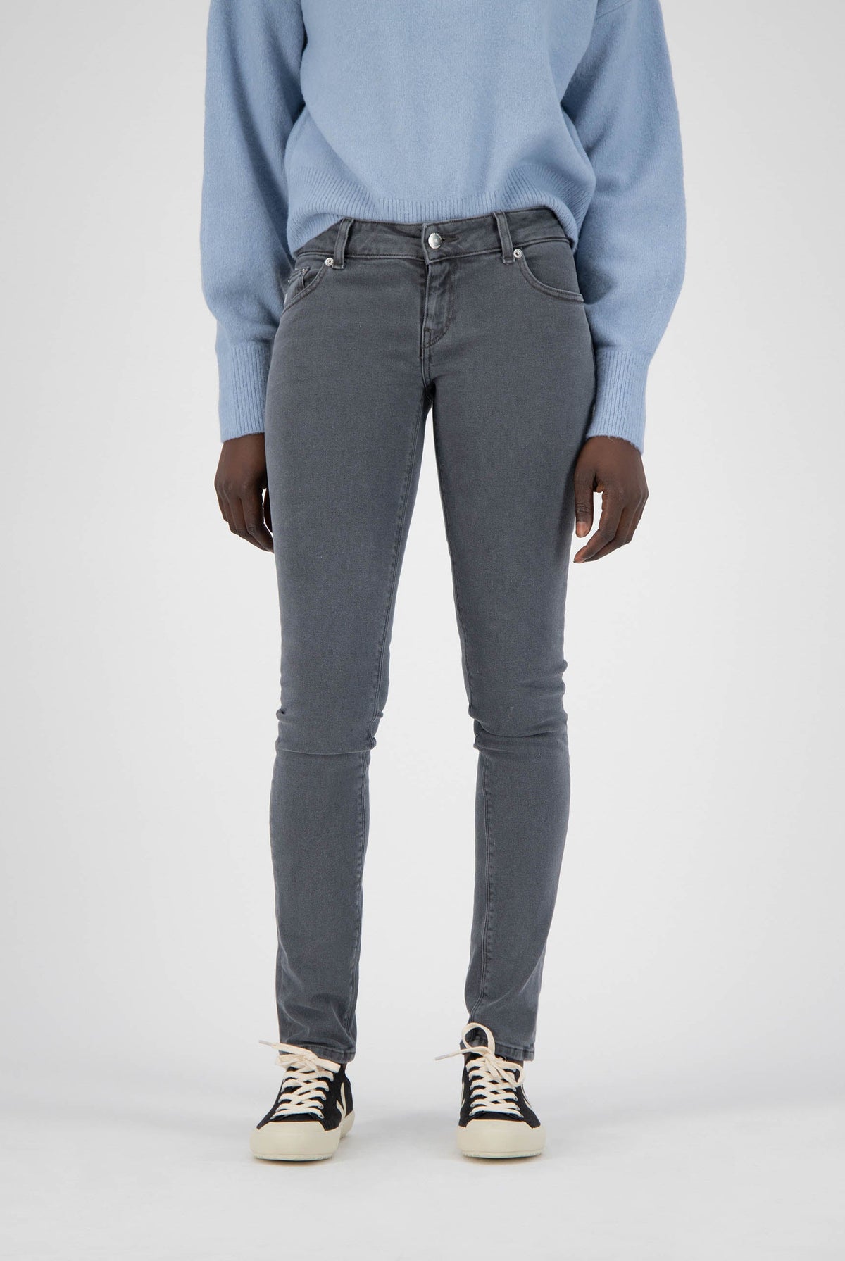 A model wearing slim-fit gray jeans paired with black and white sneakers and a cozy light blue sweater.