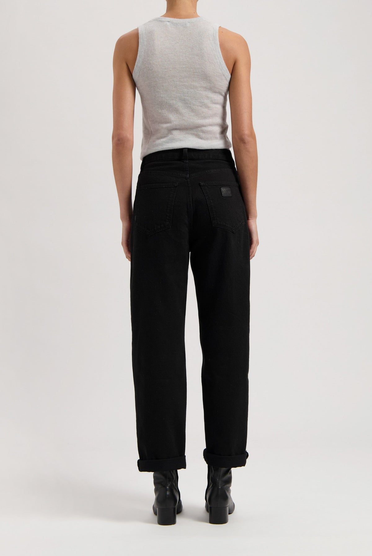 Back view of model wearing black high-waisted jeans paired with a gray sleeveless top, showcasing modern casual fashion style.