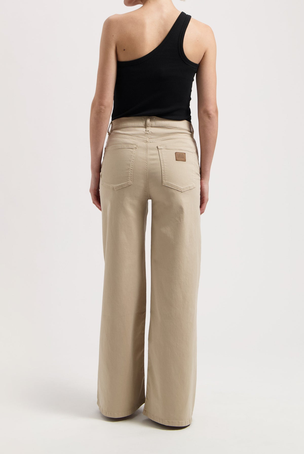 Wide-leg beige MUD Jeans made from organic cotton, worn with a black, one-shoulder sleeveless top in a minimalist style.