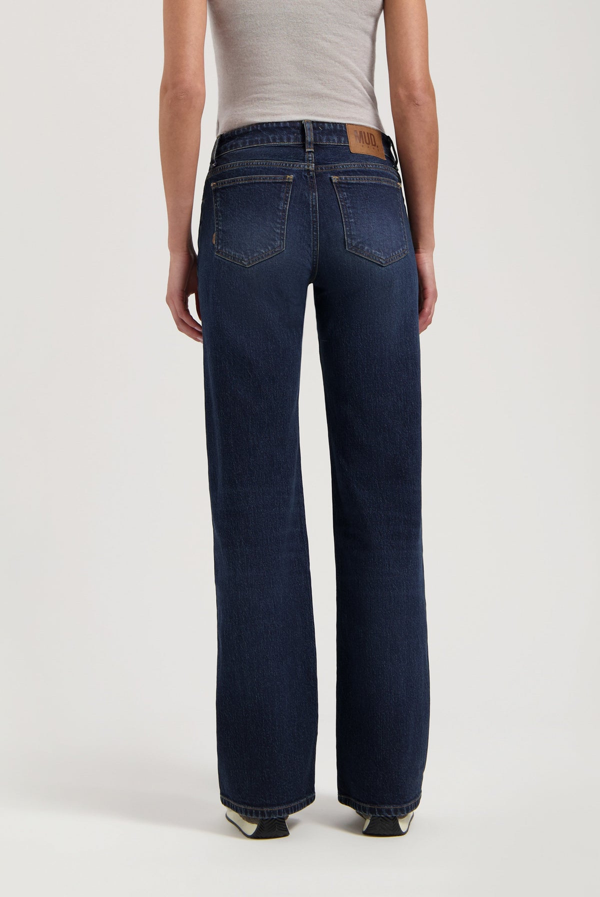 Back view of dark blue sustainable jeans from MUD Jeans, featuring a wide-leg style, paired with a fitted beige tank top.