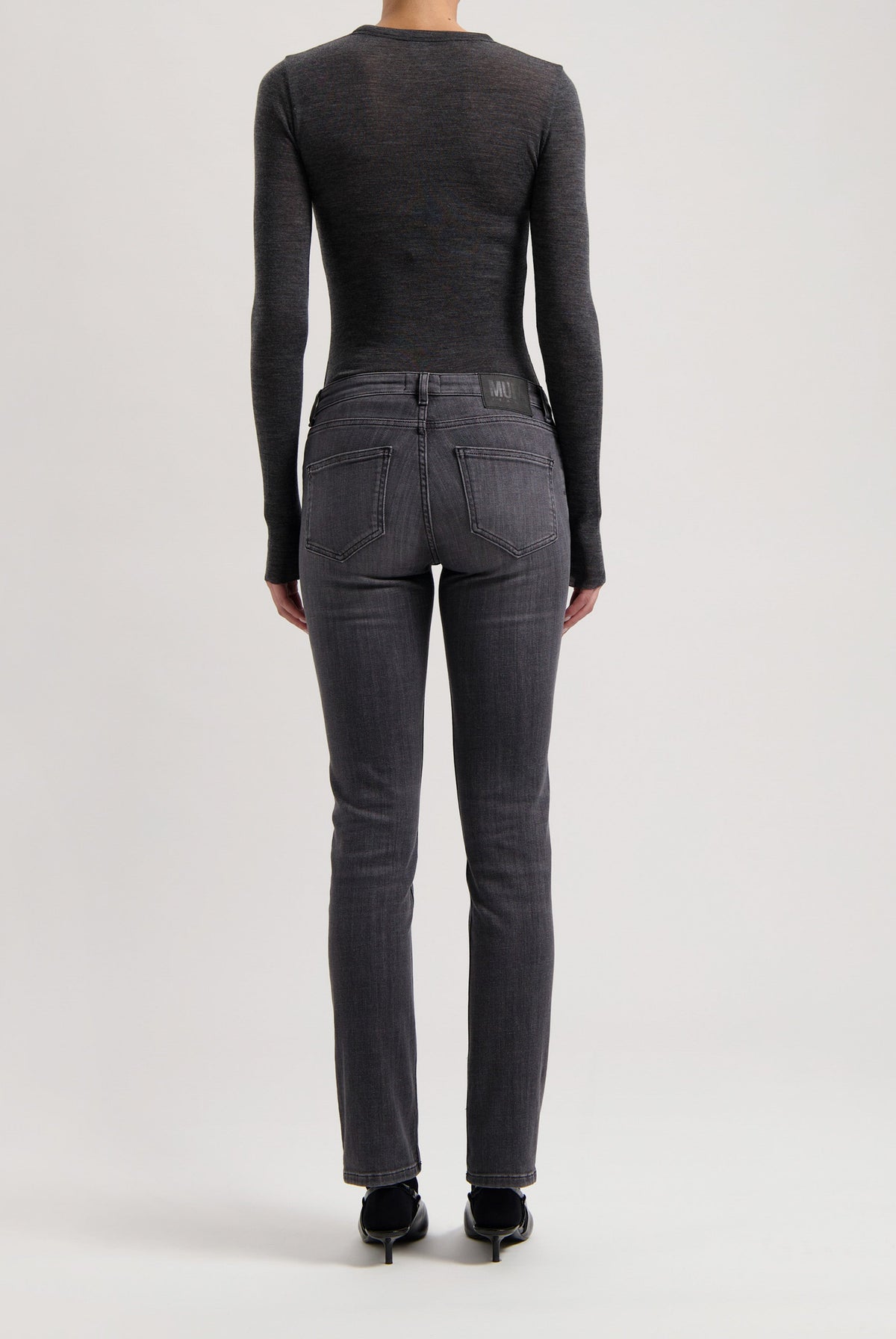 Back view of dark gray slim-fit denim jeans with a fitted long-sleeve charcoal top, highlighting sleek and modern fashion.