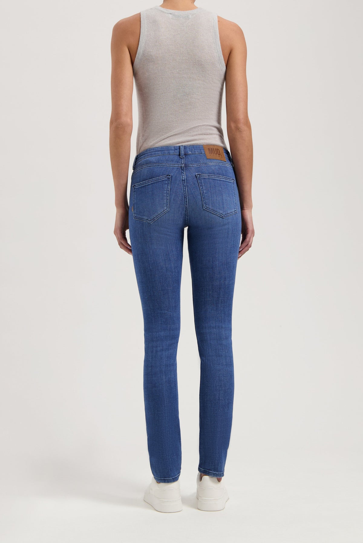 Back view of person wearing straight-fit MUD Jeans in classic blue denim, with a sleeveless gray top and white sneakers.