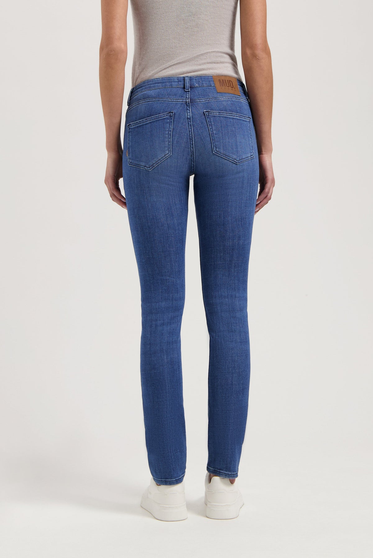 Back view of blue denim slim-fit jeans by MUD Jeans, made from organic cotton, paired with a light gray sleeveless top.