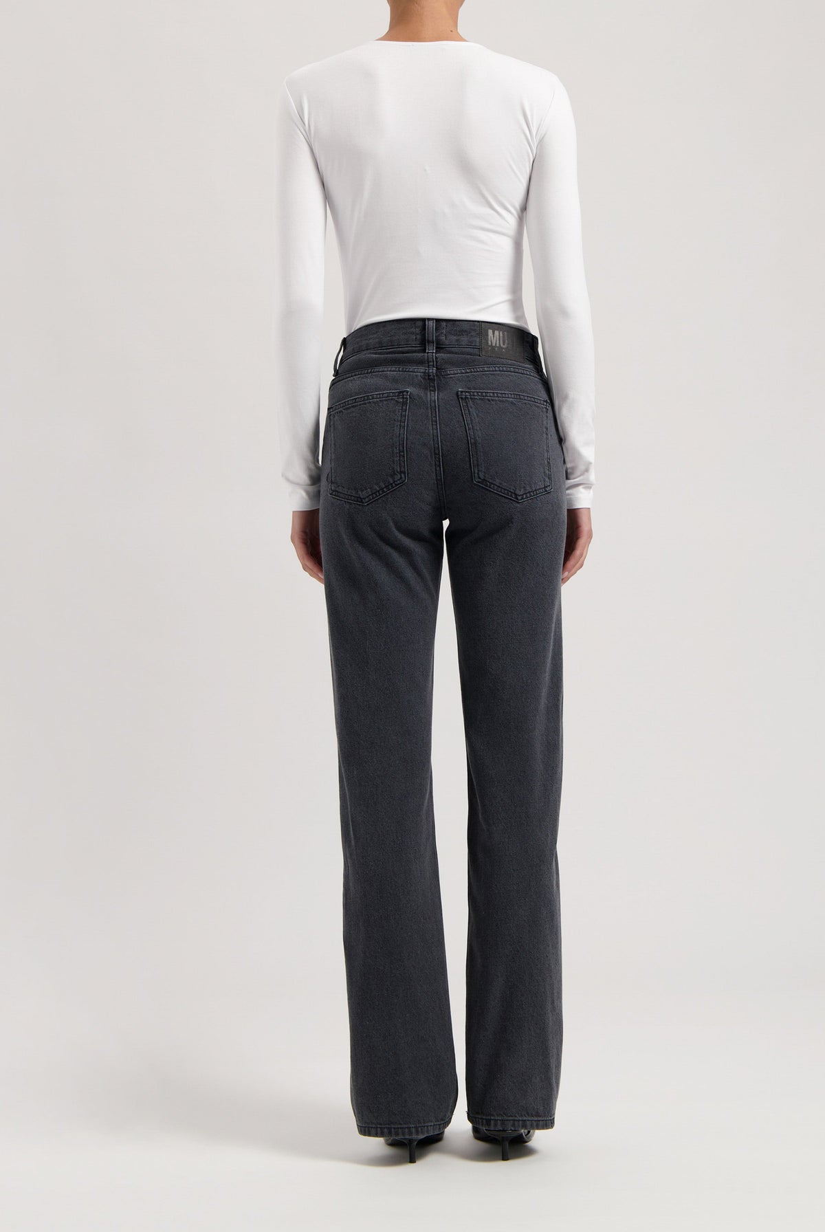 Person wearing dark gray straight-leg jeans with a high waist, paired with a fitted long-sleeve white top, viewed from the back.