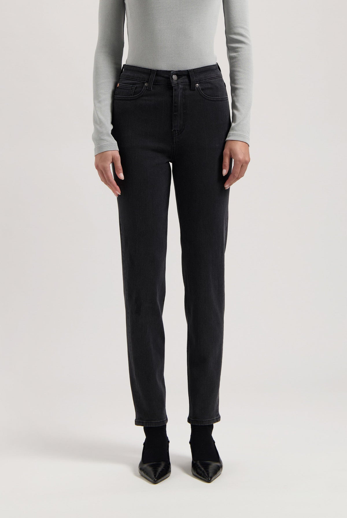 Person wearing black straight-leg jeans with a high-waist fit, paired with a light gray long-sleeve shirt and black heels.