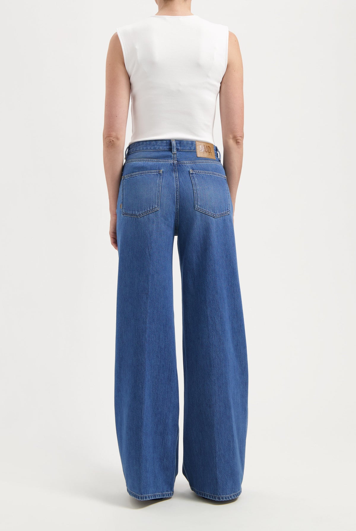 High-waisted wide-leg jeans in classic blue denim, worn with a sleeveless white top, showcasing casual style.