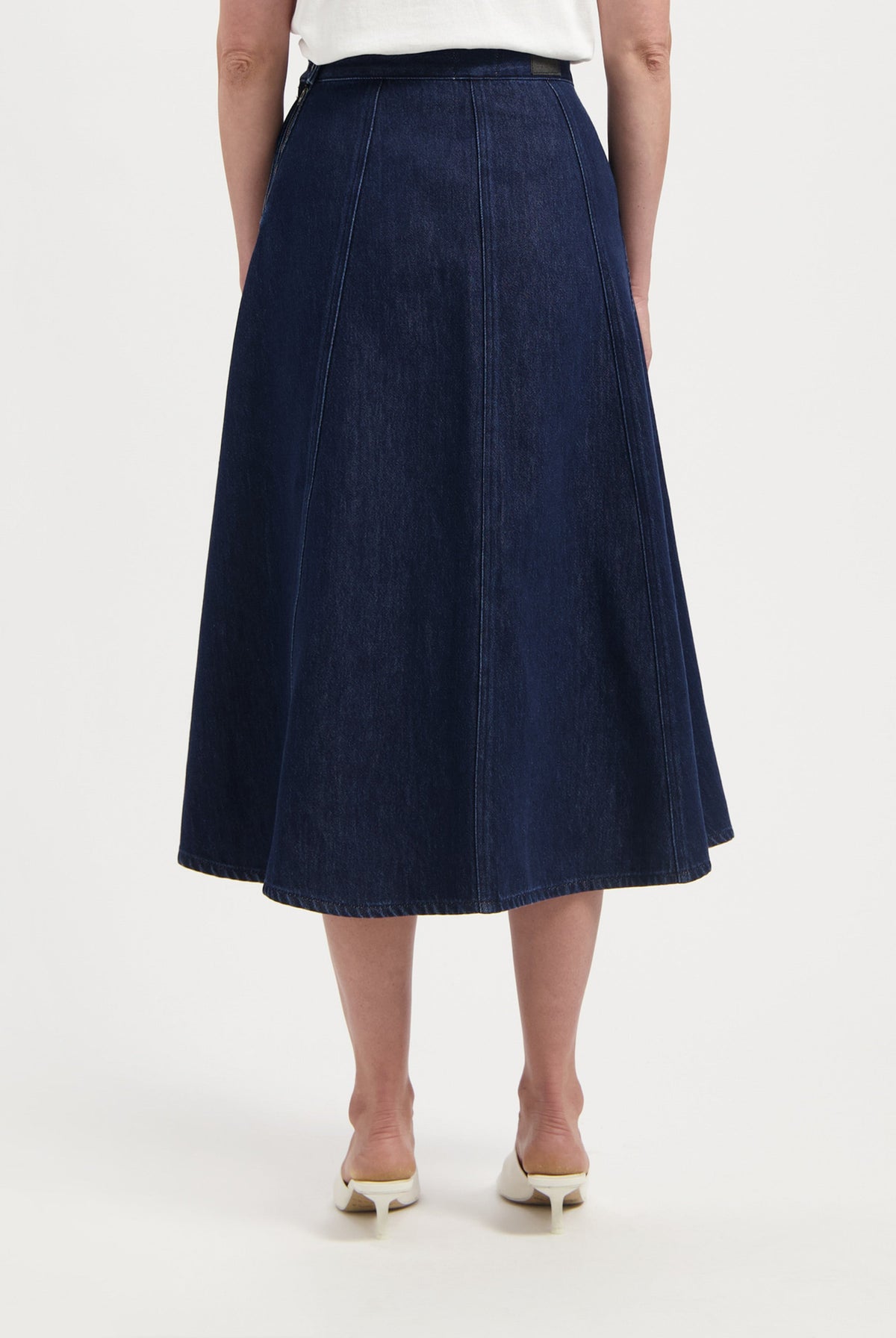 Dark blue denim A-line skirt with seam detailing, worn with a white top, highlighting the skirt's high-waisted fit and flow.