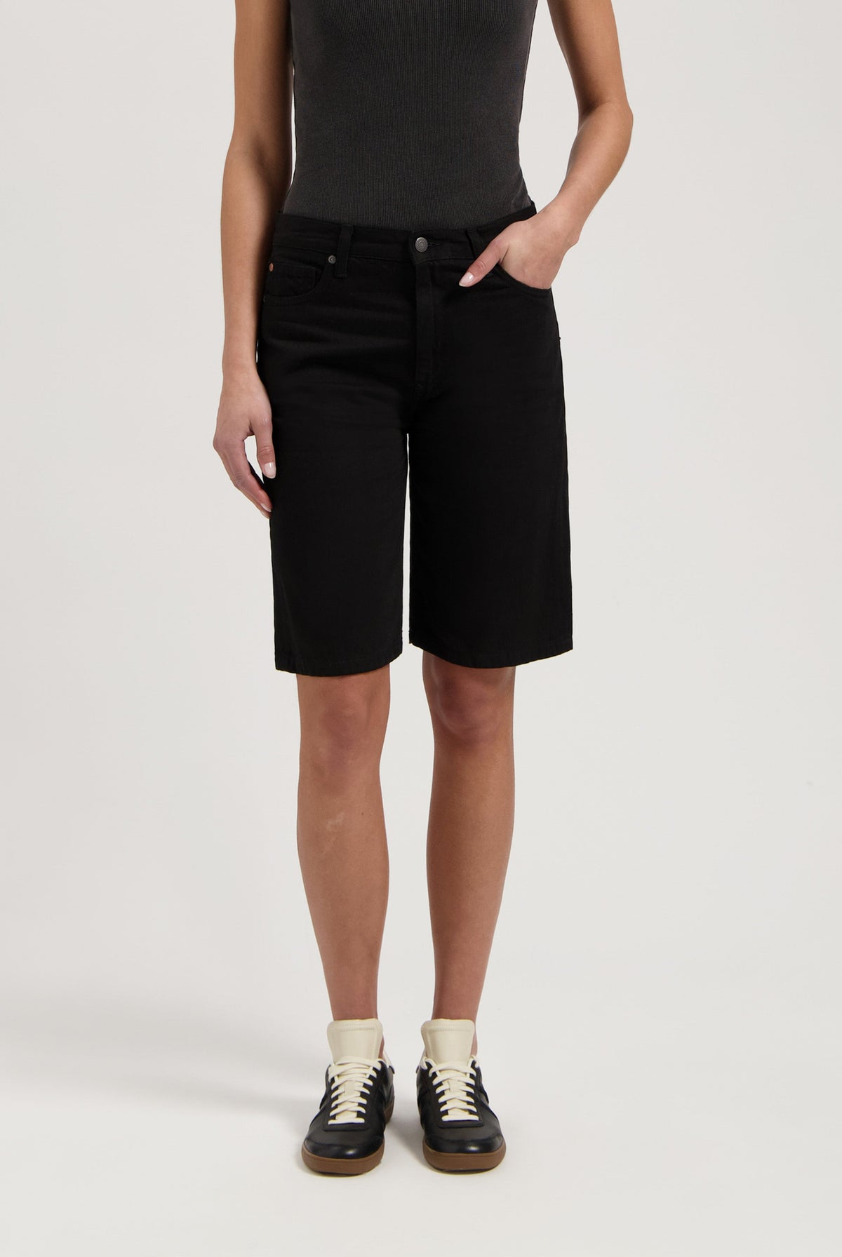 Black denim Bermuda shorts paired with a dark gray sleeveless top, worn with black and white sneakers.