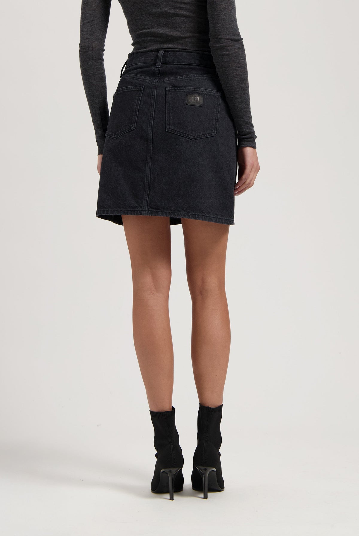 Dark denim skirt with back pockets paired with a long-sleeve gray top and black high-heeled ankle boots.
