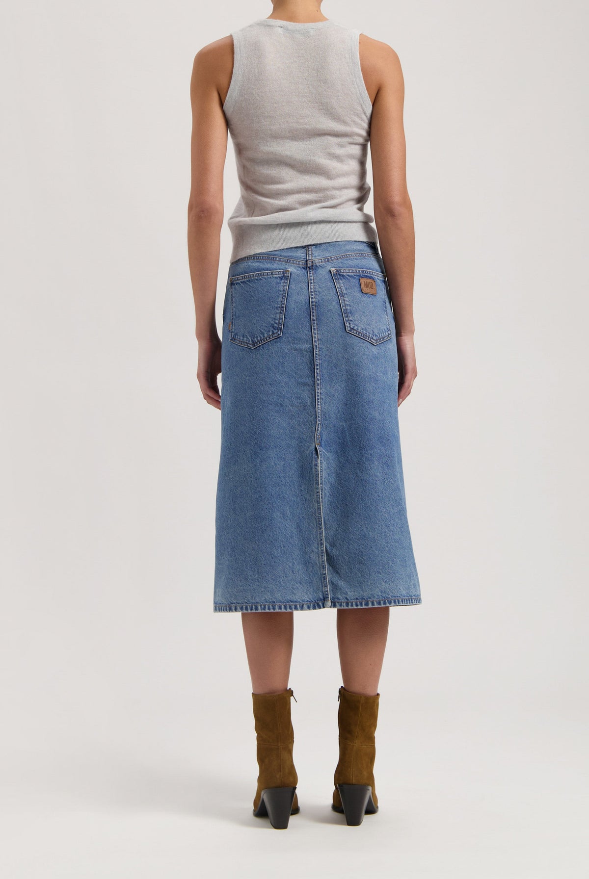 Back view of a light gray sleeveless top paired with a knee-length denim MUD Jeans skirt and brown suede ankle boots.