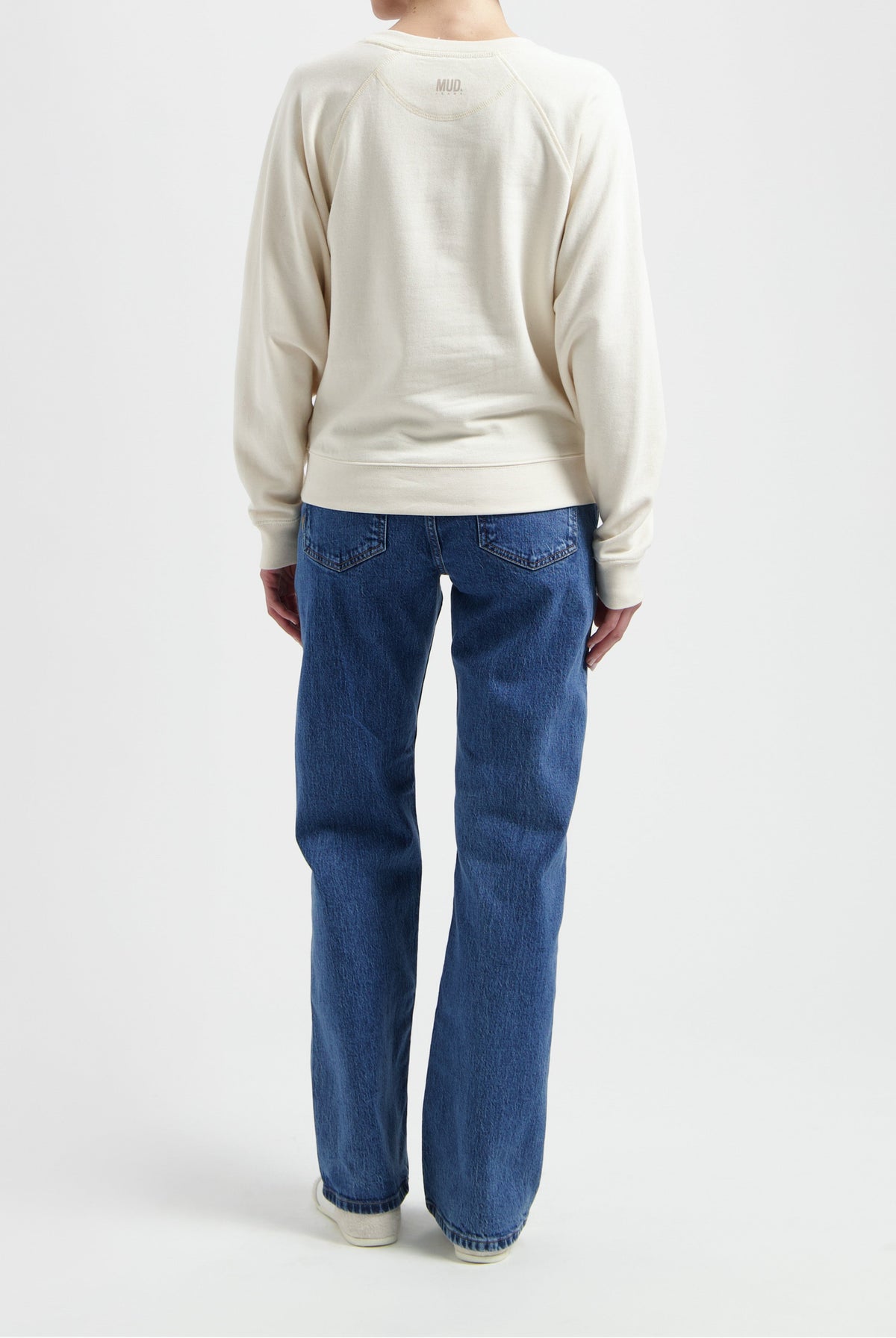 Back view of person wearing MUD Jeans, vintage blue denim, paired with cream organic cotton sweatshirt, showcasing relaxed fit style.