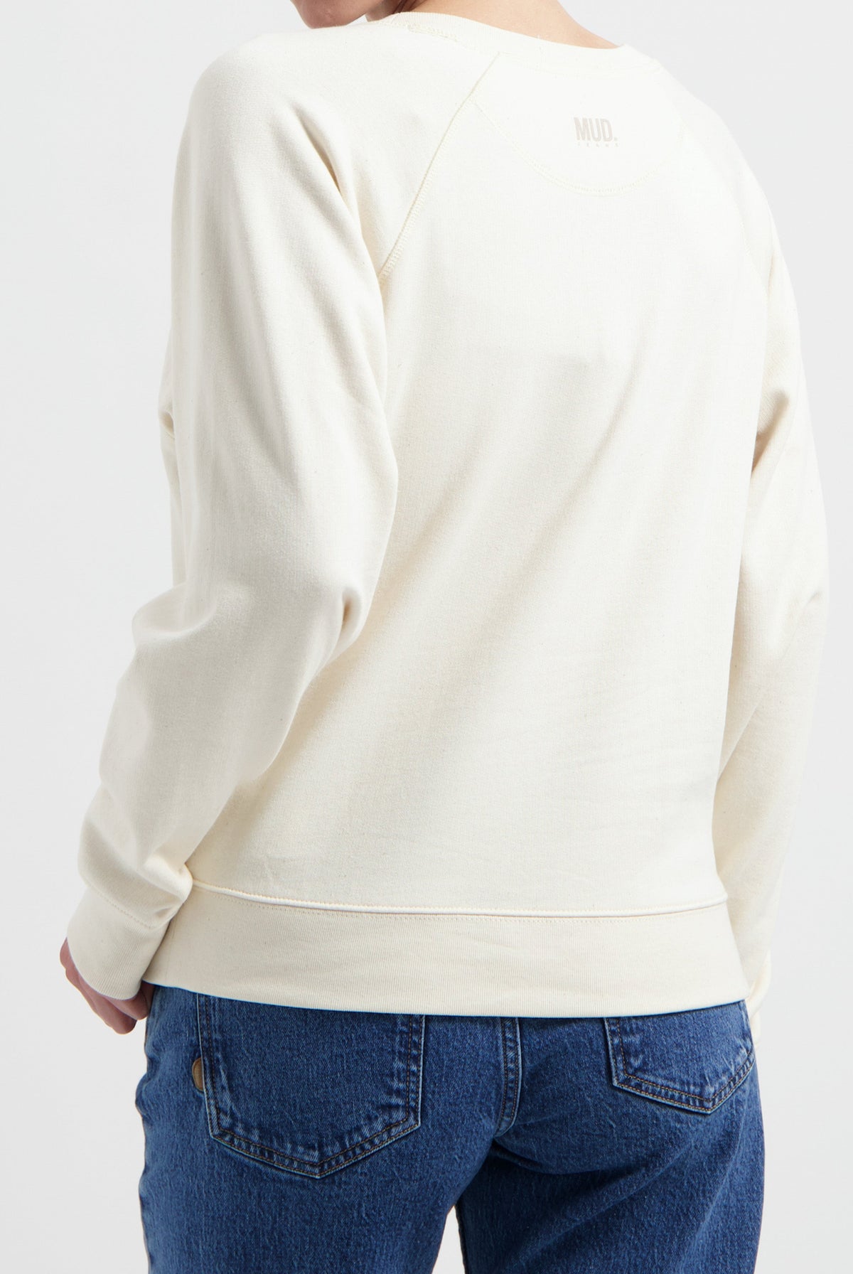 Off-white MUD sweatshirt paired with blue denim jeans, showcasing a sustainable fashion choice with relaxed fit and style.