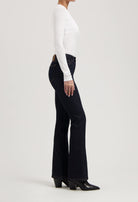 Model wearing dark blue flare jeans paired with a fitted white long-sleeve top and black heeled ankle boots.