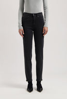 Person wearing black straight-leg jeans with a high-waist fit, paired with a light gray long-sleeve shirt and black heels.